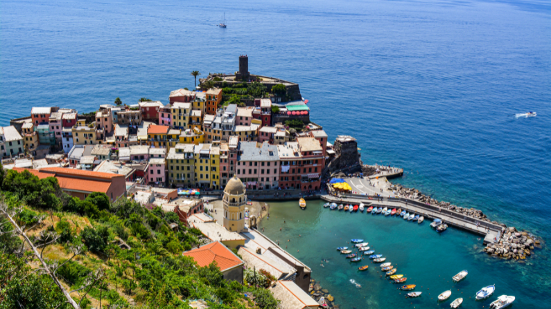 Views from atop the cliffs above a small, colorful fishing village in coastal Italy surrounded by blue water and small harbor