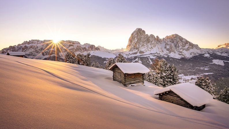 Snowy hillside with cabins. Mountains in the background during winter in Val Gardena